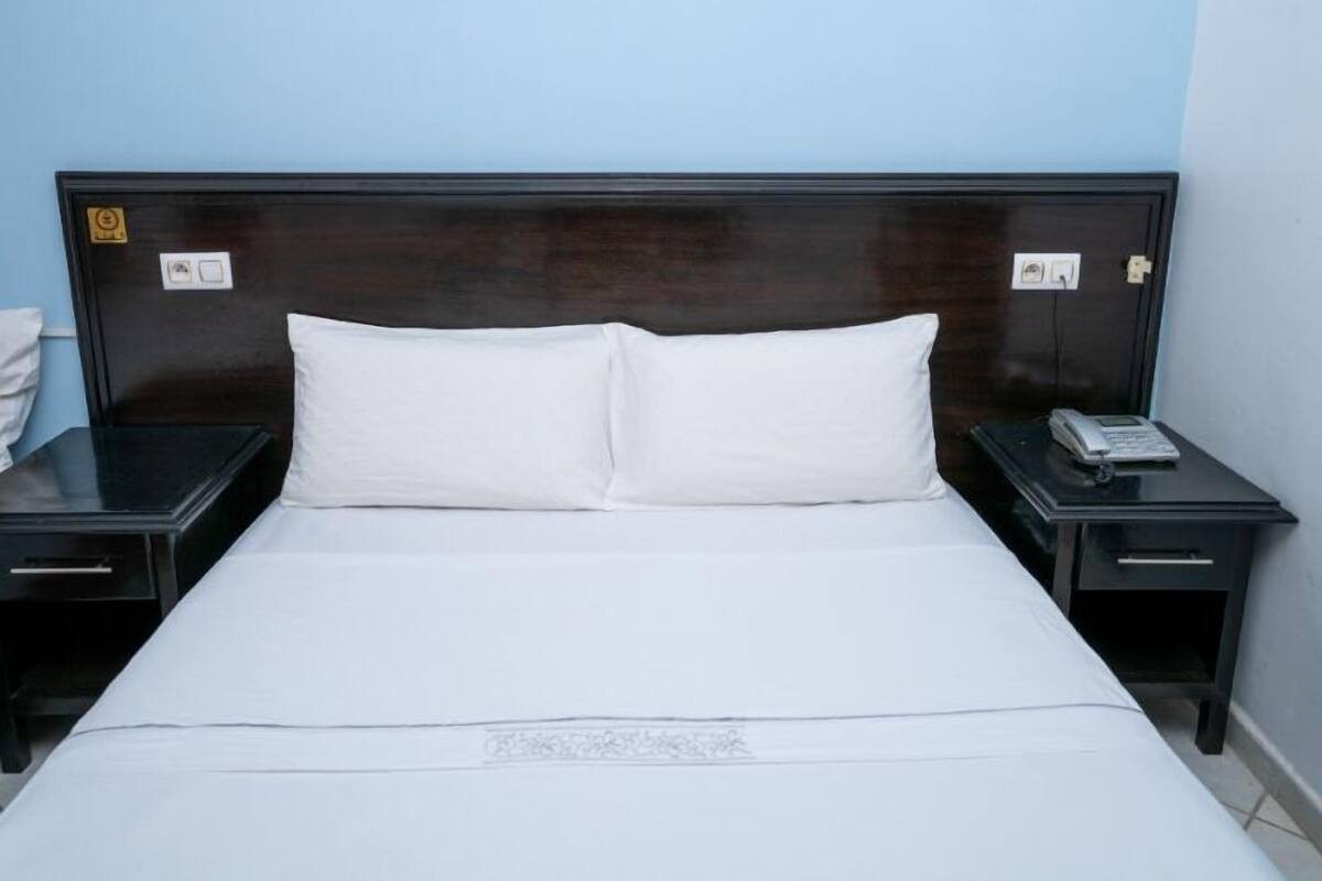 Habitación de hotel con cabecera de madera oscura, ropa de cama blanca y teléfono en la mesita de noche.