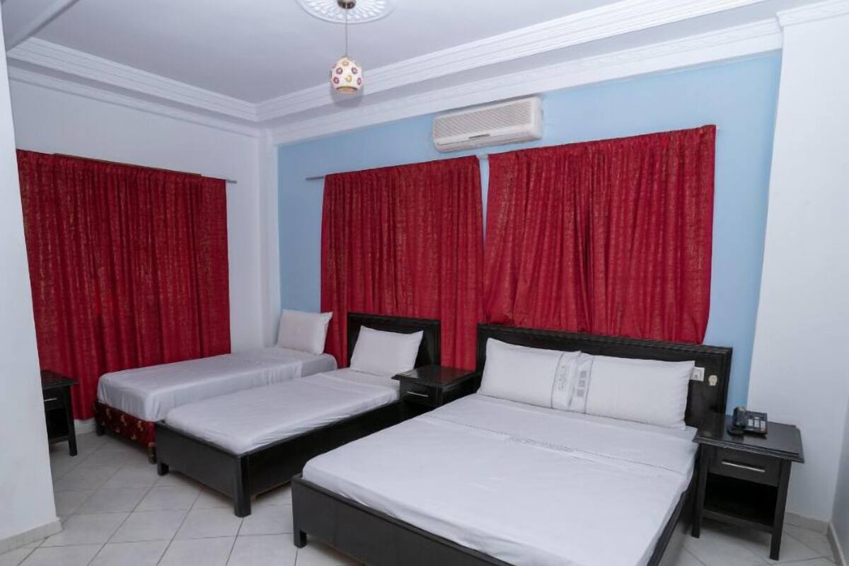 Habitación de hotel con dos camas individuales, una cama grande y una mesita de noche con teléfono.