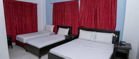 A hotel room with two single beds, a large bed, and a nightstand with a phone.