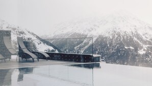 A modern infinity pool with a glass barrier, surrounded by snow-covered mountains. - Hotel Schöne Aussicht (Soelden)