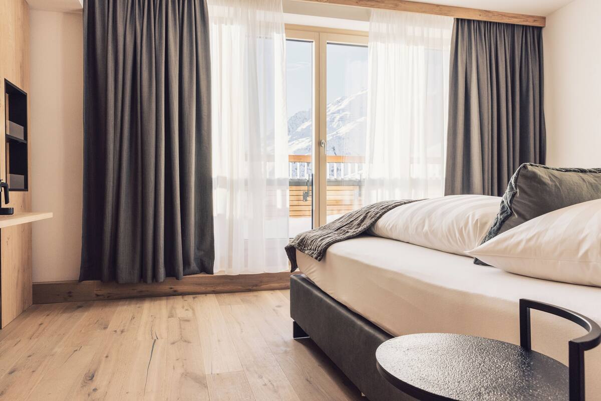 A modern bedroom with a bed, a round table, and a view of mountains through the window.
