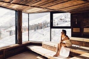Une cabane en bois dotée de grandes fenêtres donnant sur un paysage montagneux enneigé.