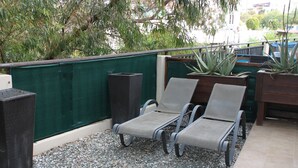 Een terras op het dak met twee loungestoelen, een bijzettafeltje en een plantenbak met planten.