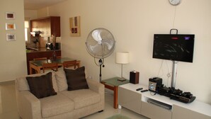 En stue med sofa, ventilator, fjernsyn og et lille bord med lampe.