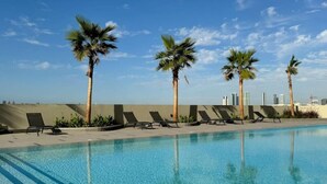A swimming pool with palm trees and lounge chairs. - Two Bedroom: Modern and Chic with Balcony (Jumeirah Village Triangle)