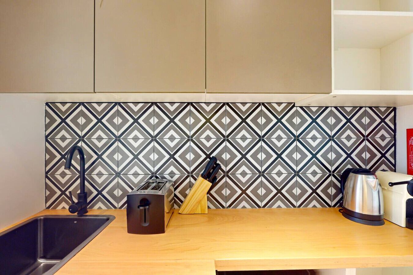 Eine Küche mit modernem Design, mit einer Rückwand in geometrischem Muster, einem Edelstahl-Spülbecken, einem Toaster, einem Messerblock und einem Wasserkocher auf der Arbeitsfläche.