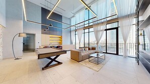 Una sala de estar moderna con billar, un sofá y una mesa de centro. Hay un ventanal con cortinas y vistas a la ciudad.