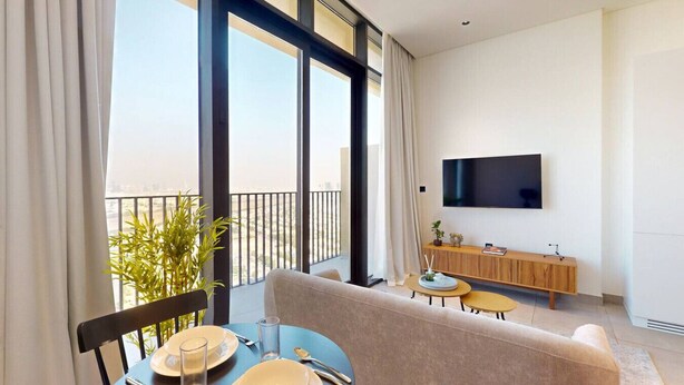 Ein modernes Hotelzimmer mit Balkon, einem an der Wand montierten Fernseher und einer Essecke mit Tisch für zwei Personen.