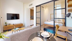 Ein modernes Hotelzimmer mit Bett, Fernseher, einer Essecke und einer Schiebetür zu einem Badezimmer.