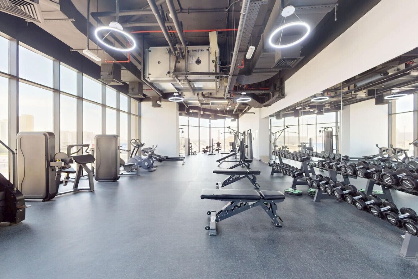 Ein Fitnessstudio mit unterschiedlichen Trainingsgeräten, großen Fenstern und hoher Decke.