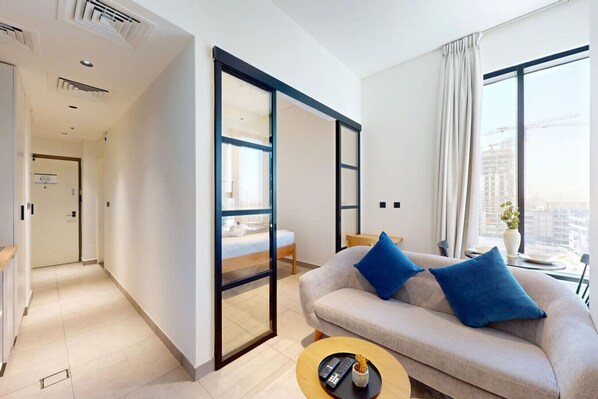 Una habitación de hotel moderna con sofá, mesa de centro, cama con puerta corredera y vista a la ciudad a través de grandes ventanales.