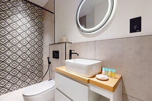 Un baño moderno con un lavabo blanco, un espejo y artículos de aseo en la encimera.
