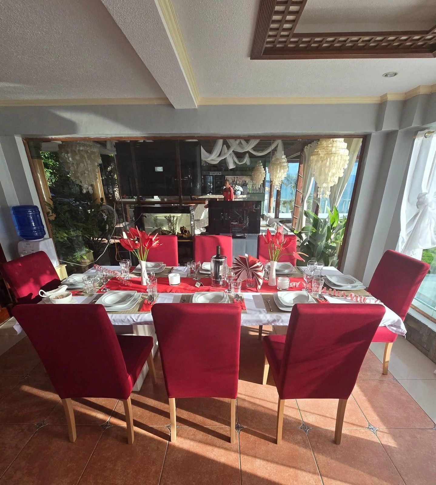 A dining area with a large table set for six, red chairs, and a view of the outdoors.