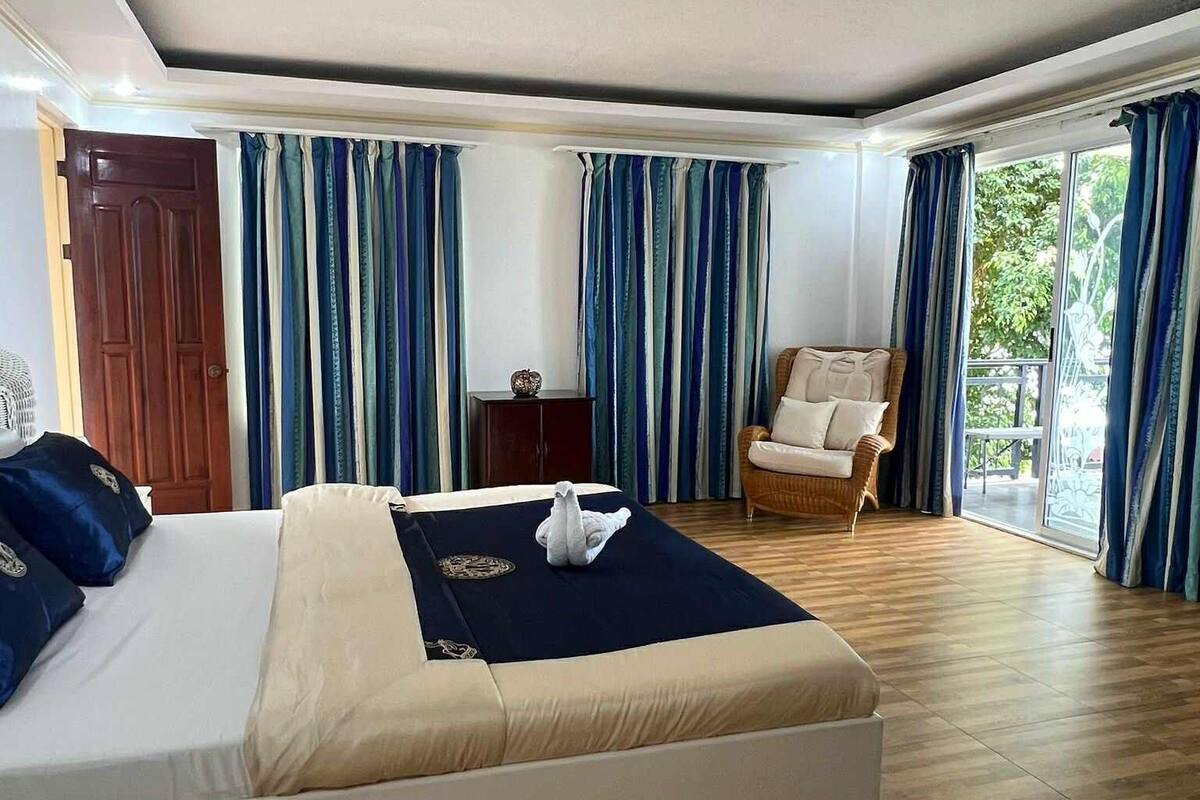 Ein geräumiges Schlafzimmer mit einem großen Bett, einem Sessel und Blick ins Freie durch eine Schiebetür.