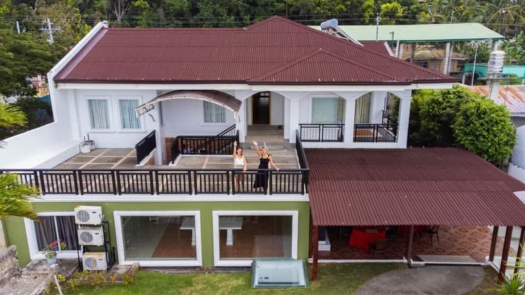 Ein zweistöckiges Haus mit Balkon, großen Fenstern und einer überdachten Veranda.