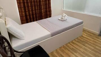 Habitación individual con cama individual, piso de madera, cama blanca, silla marrón, ventana con persiana y cortina.