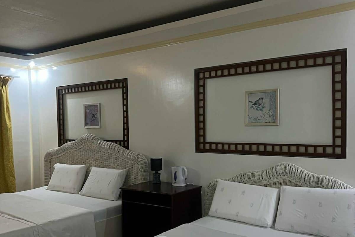 Ein Hotelzimmer mit zwei Einzelbetten, einem Nachttisch mit Lampe und Wasserkocher sowie einem gerahmten Bild an der Wand.