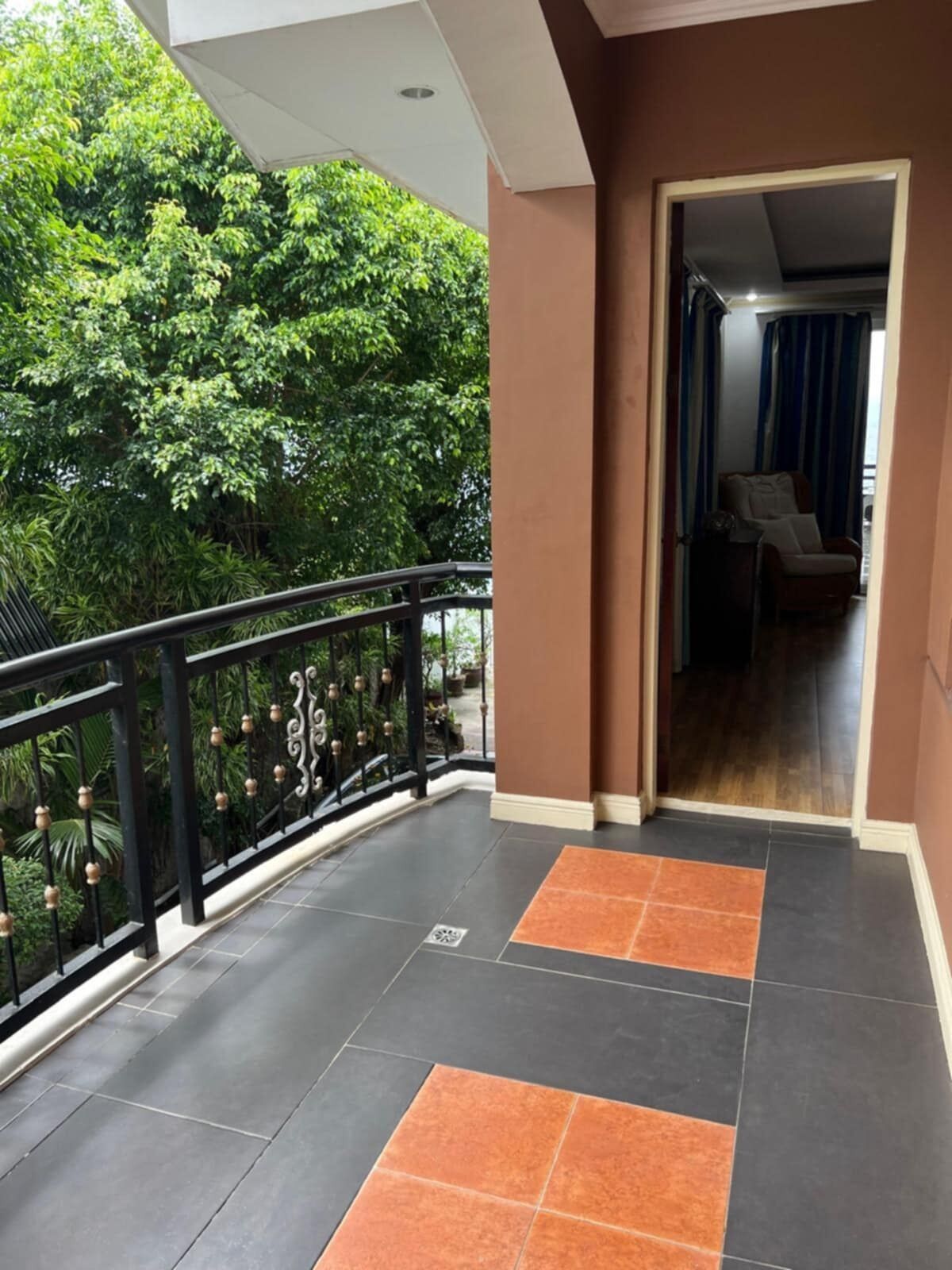 Un balcon doté d’une balustrade noire, offrant une vue sur une végétation luxuriante, et un sol carrelé agrémenté de touches de couleur orange.