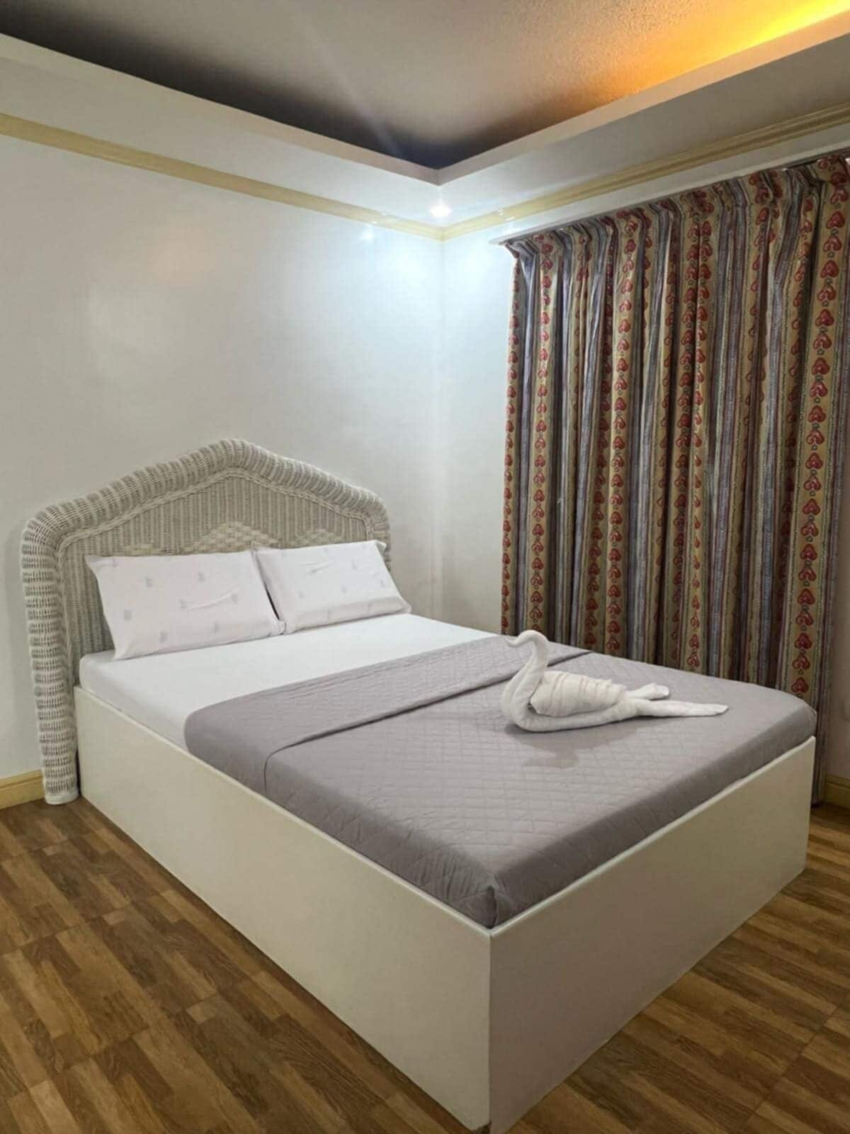 A neatly made bed with a grey quilt and white pillows, a white headboard, and a wooden floor.