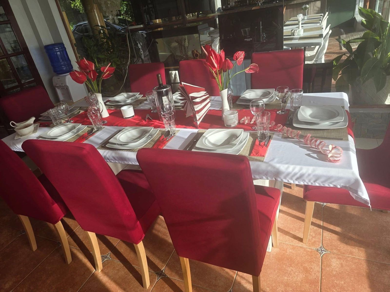Mesa de comedor lista para seis personas, con sillas rojas, mantel blanco y servilletas rojas.
