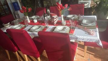 Mesa de comedor lista para seis personas, con sillas rojas, mantel blanco y servilletas rojas.