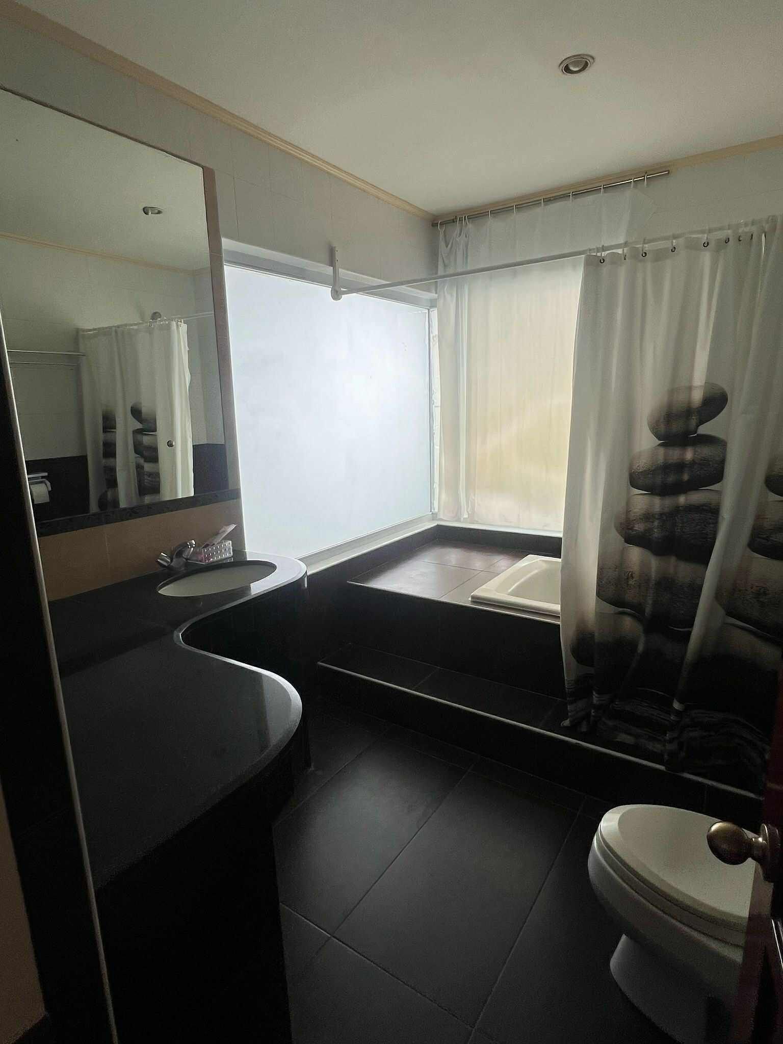 A modern bathroom with a large mirror, a sink, a bathtub, and a toilet.