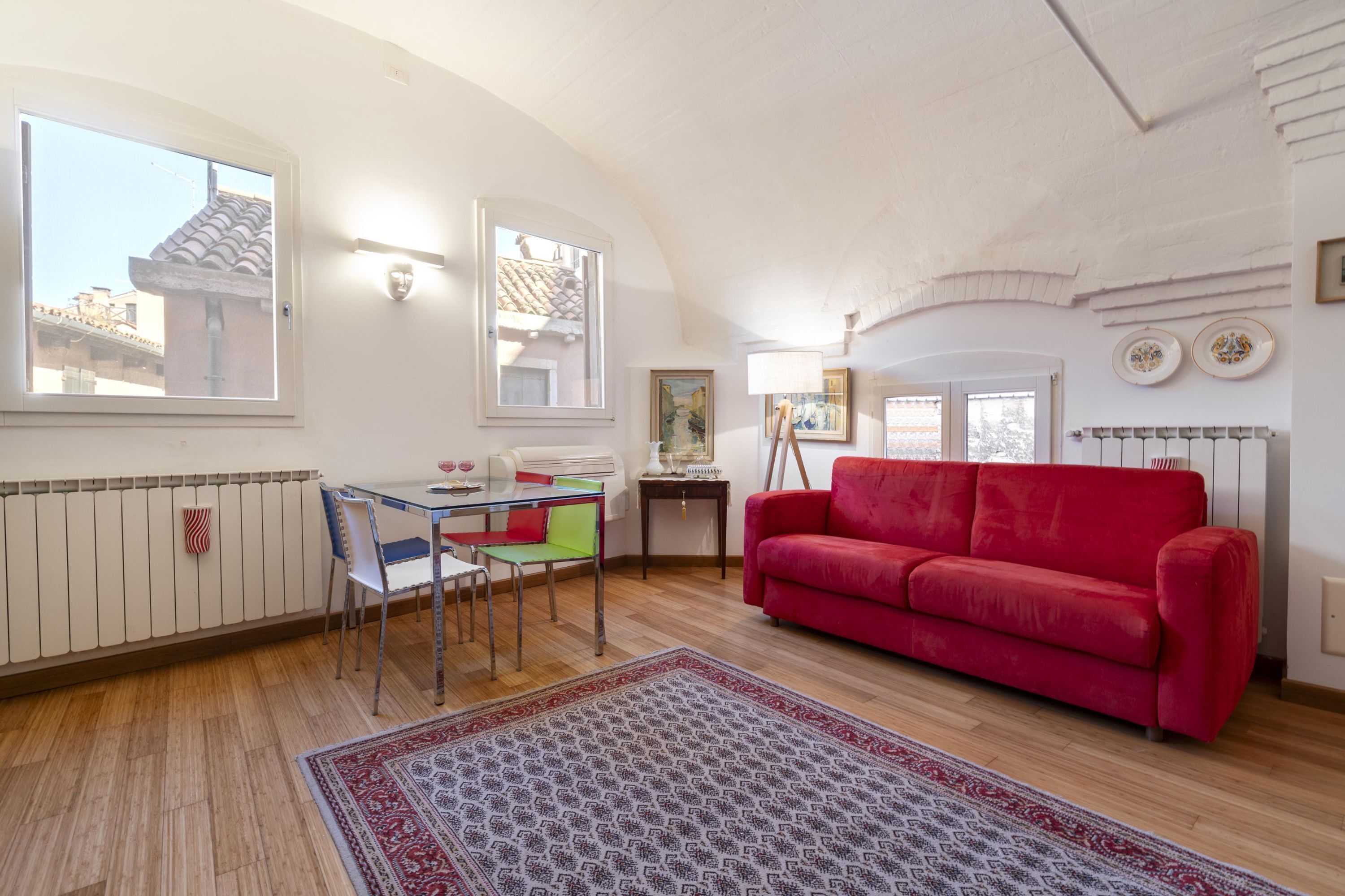 Une pièce avec un canapé rouge, une table à manger avec des chaises, un tapis à motifs et un radiateur.