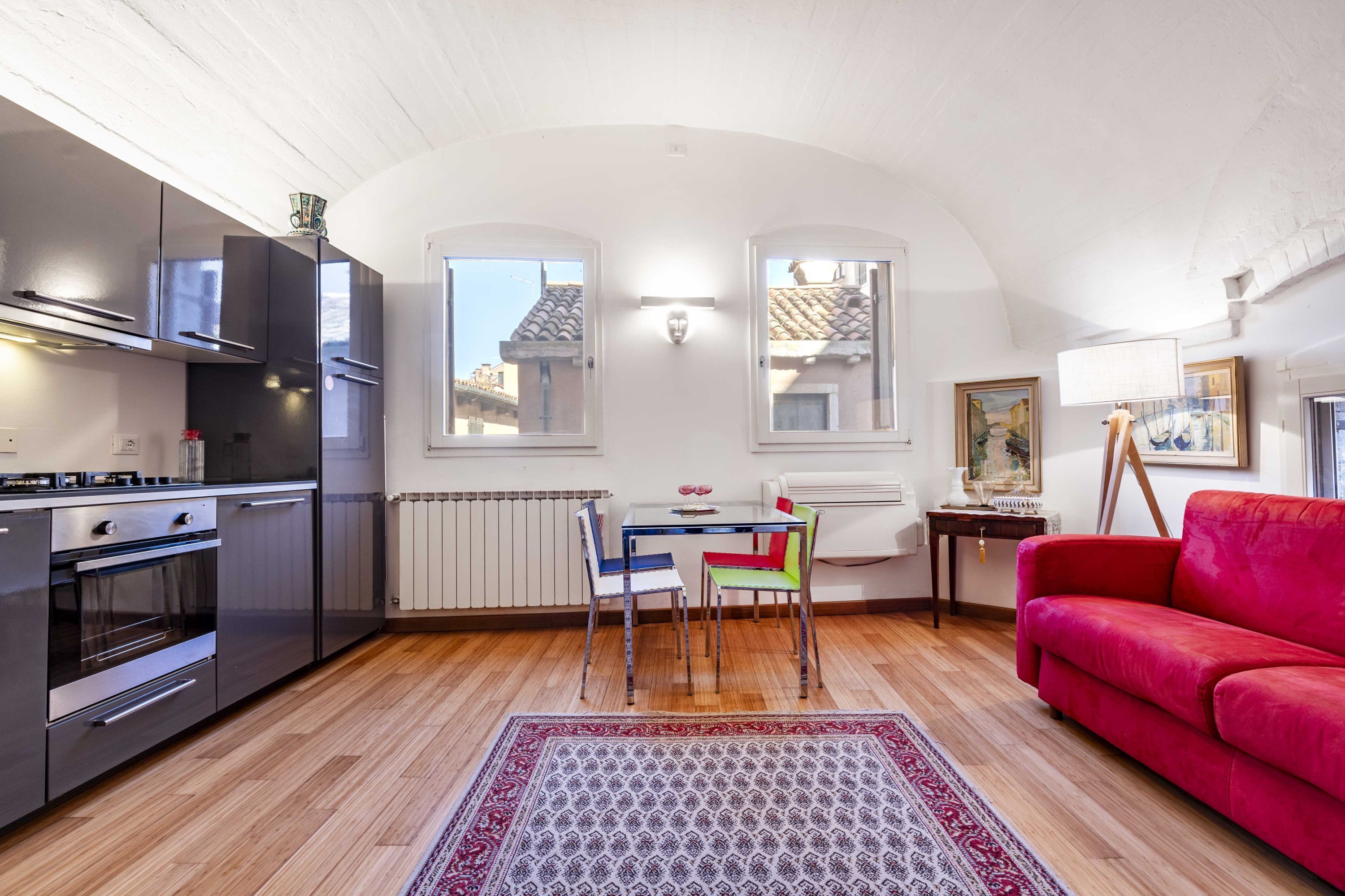 A compact living space with a kitchenette, a dining area with chairs, a red sofa, and a patterned rug.