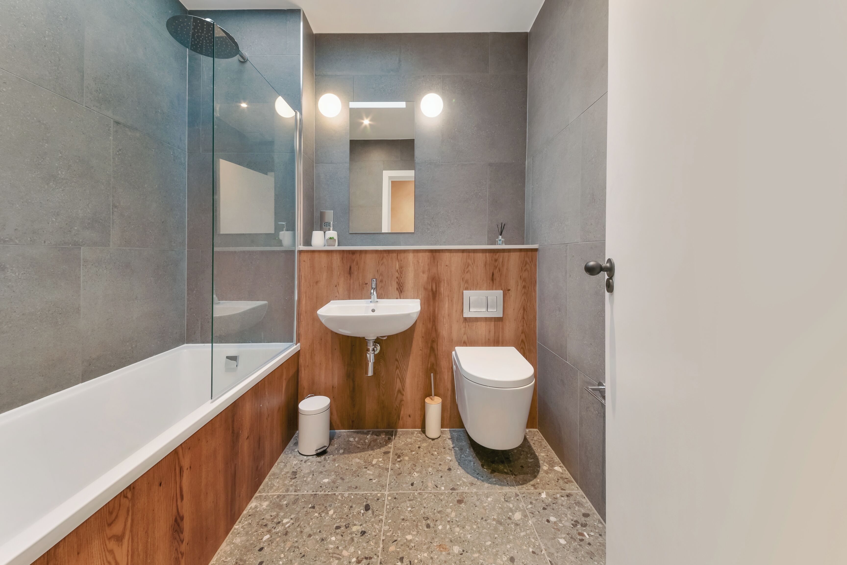 A modern bathroom with a glass-enclosed shower, a wooden vanity, a white sink, and a toilet.