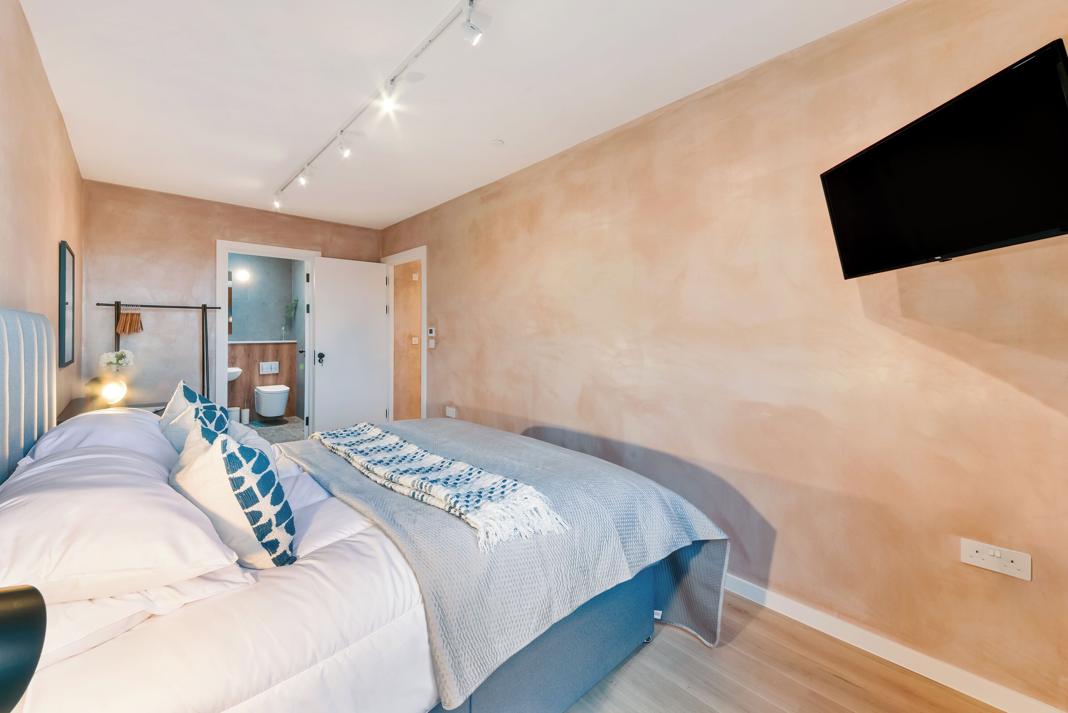 A bedroom with a bed, a TV mounted on the wall, and a bathroom visible through an open door.