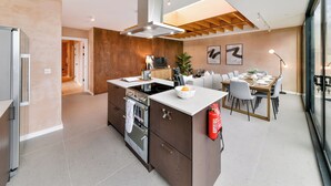 Een moderne keuken met een centraal eiland, een ingebouwde oven en een eethoek met een tafel en stoelen.