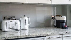 Una cocina con un tostador Breville, una tetera eléctrica blanca y una cafetera Krups sobre una encimera de granito.