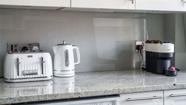 A kitchen with a Breville toaster, a white electric kettle, and a Krups coffee maker on a granite countertop.