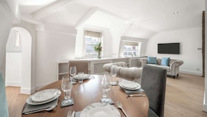 A modern loft apartment with a dining area, a sofa set, and a flat-screen TV mounted on the wall.