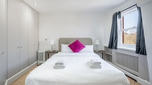 Habitación de hotel con cama, dos mesitas de noche, un radiador y una ventana con cortinas.