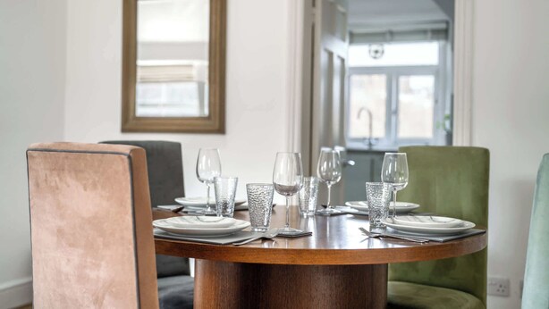 Una mesa de comedor dispuesta con platos, vasos y cubiertos, rodeada de sillas.