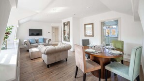 A spacious living area with a dining table set for four, a sofa, and a television mounted on the wall.