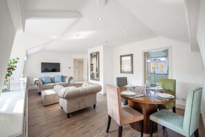 A spacious living area with a dining table set for four, a sofa, and a television mounted on the wall.