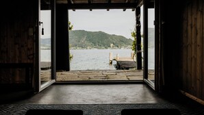 Une pièce avec vue sur un lac et des montagnes, un plancher en bois et un banc près de la fenêtre.