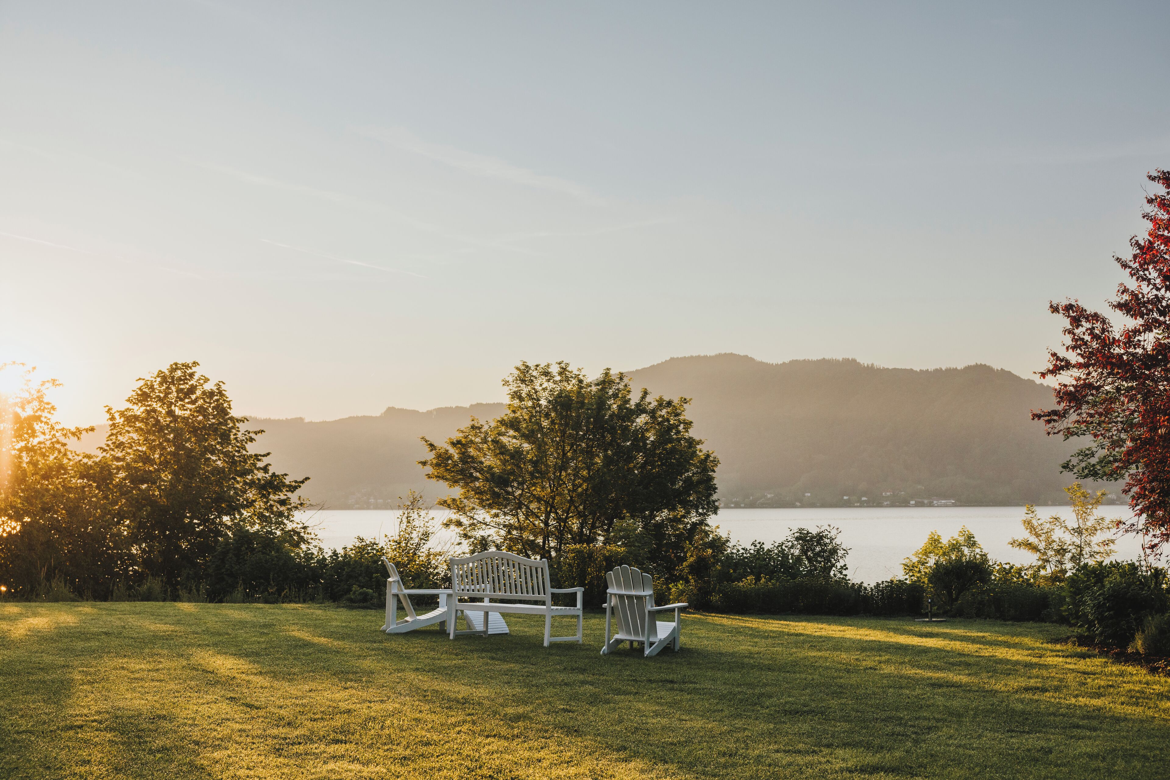 A grassy area with two Adirondack chairs facing a lake and hills in the background.