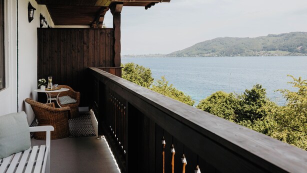 Un balcon en bois, agrémenté de meubles en osier, avec vue sur un lac.