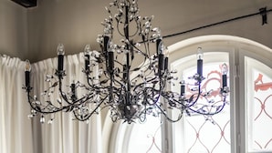 Une table à manger dressée avec différents plats, un lustre et une fenêtre ornée de ferronnerie décorative.