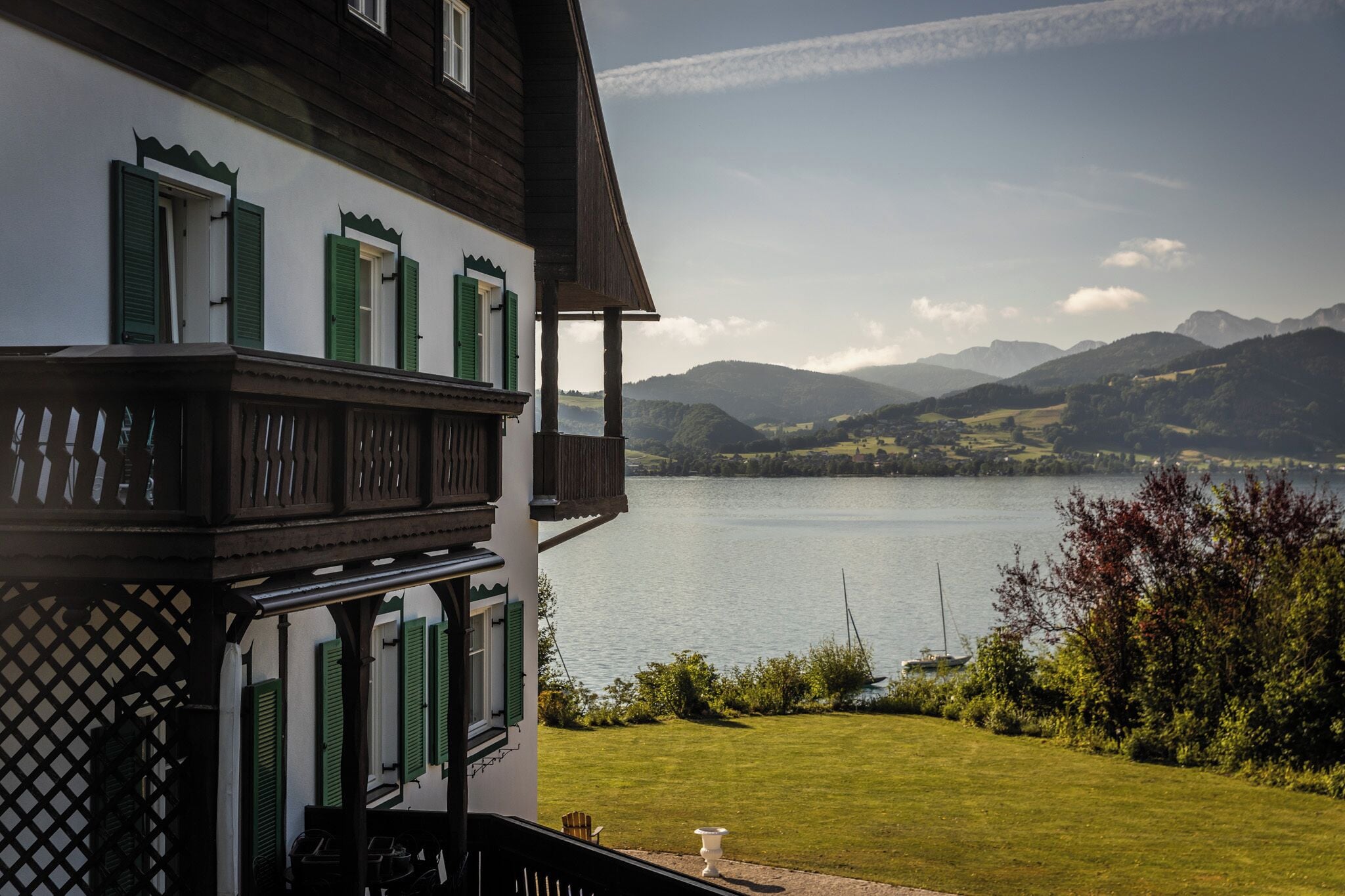 A traditional chalet with a balcony overlooking a lake and mountains.