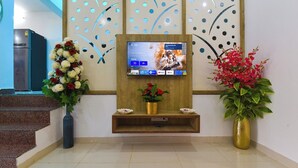 A reception area with a TV mounted on a wooden panel, a refrigerator, and decorative floral arrangements. - Villa Inn Udaipur by Yansh Group (Udaipur)