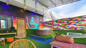 A modern outdoor lounge area with artificial grass, wicker furniture, and colorful wall art. - Villa Inn Udaipur by Yansh Group (Udaipur)