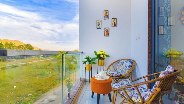 A balcony with wicker chairs, a small orange table, and potted plants. - Villa Inn Udaipur by Yansh Group (Udaipur)