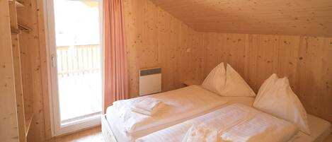 Una habitación de madera con cama, ventana con cortinas y un radiador.