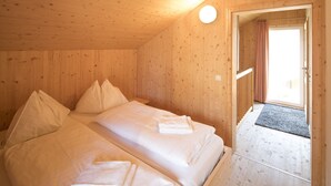 Quarto de madeira com duas camas, uma porta que dá para o exterior e uma luminária no teto.