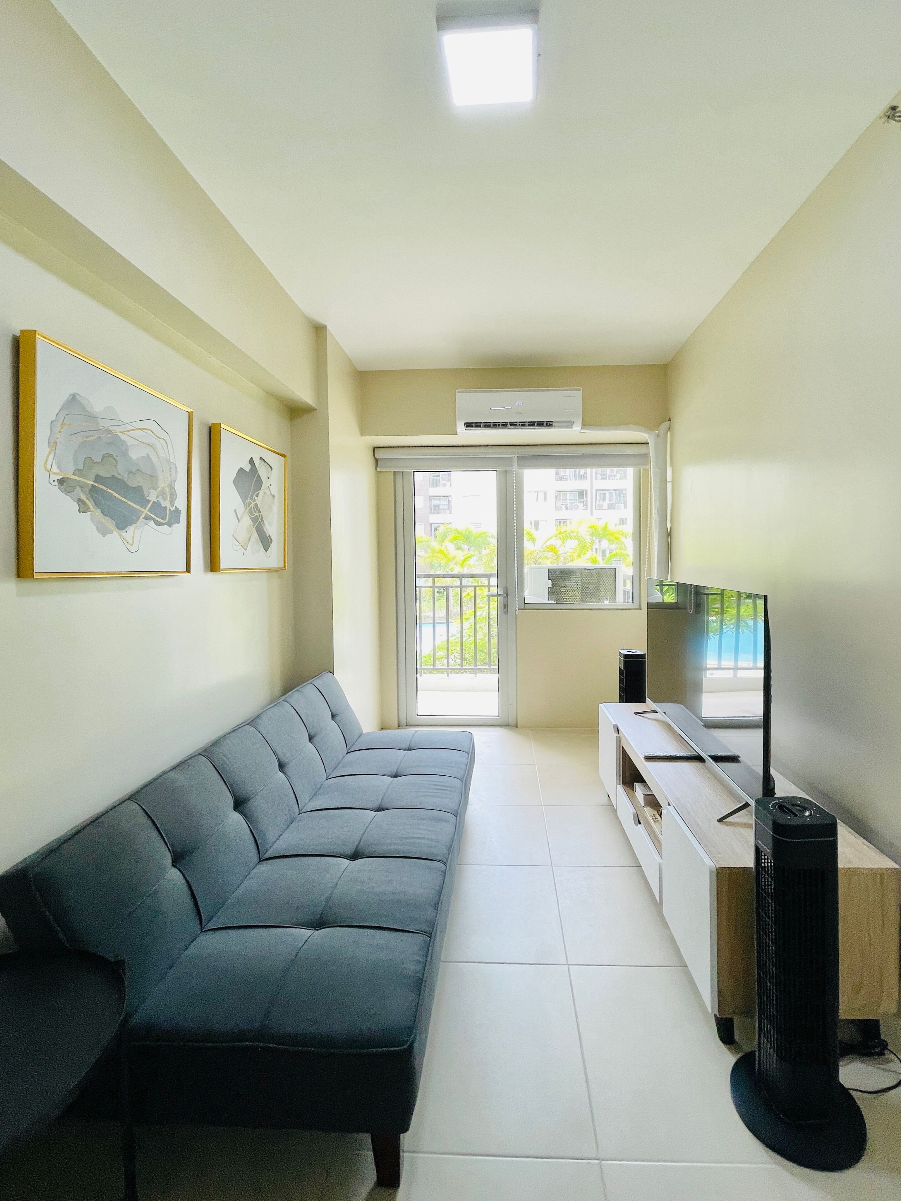 A living room with a grey sofa, a TV stand with a flat-screen TV, and two framed abstract artworks on the wall.