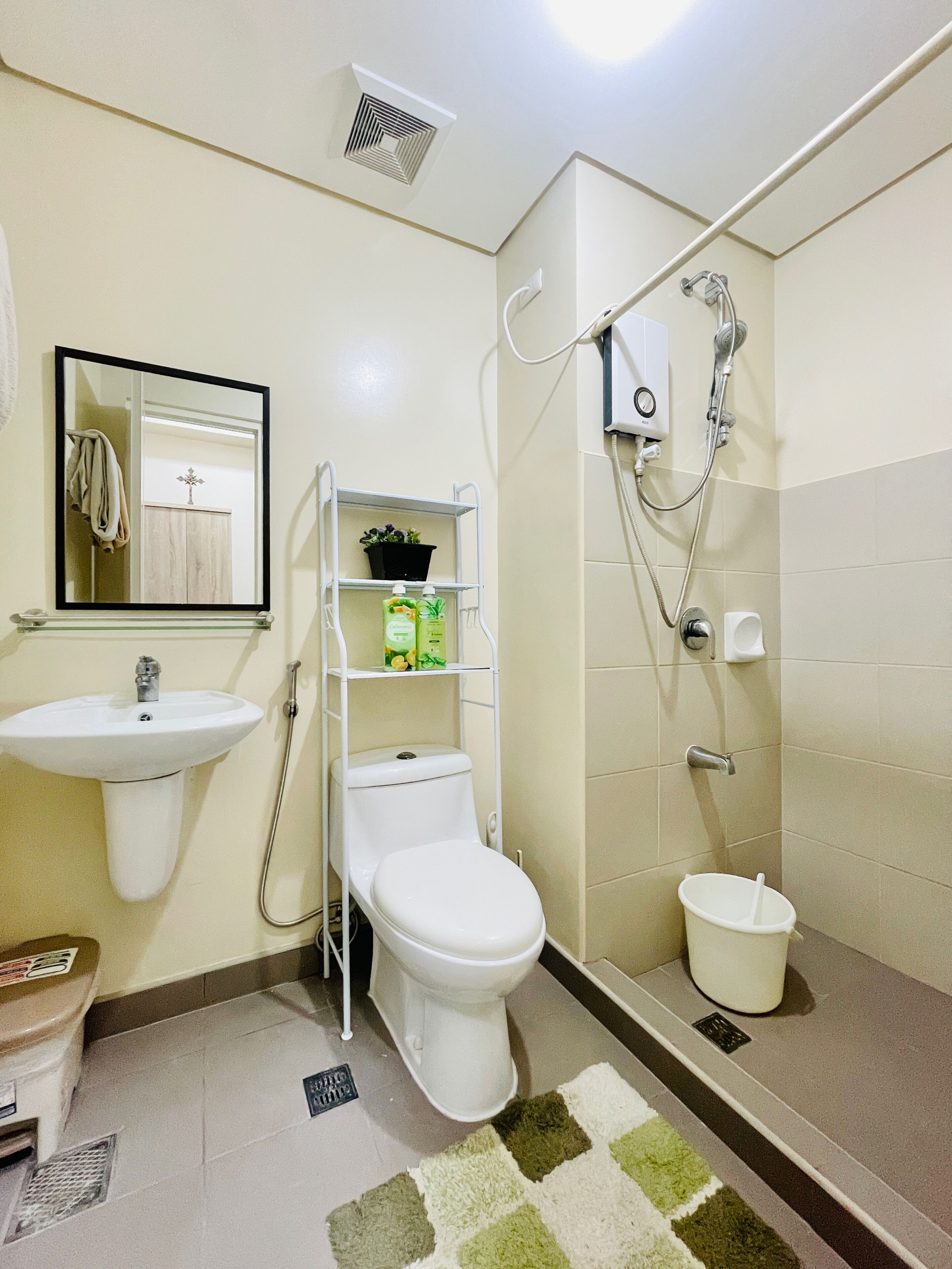 A bathroom with a sink, toilet, and shower. There is a shelf with toiletries and a mirror above the sink.